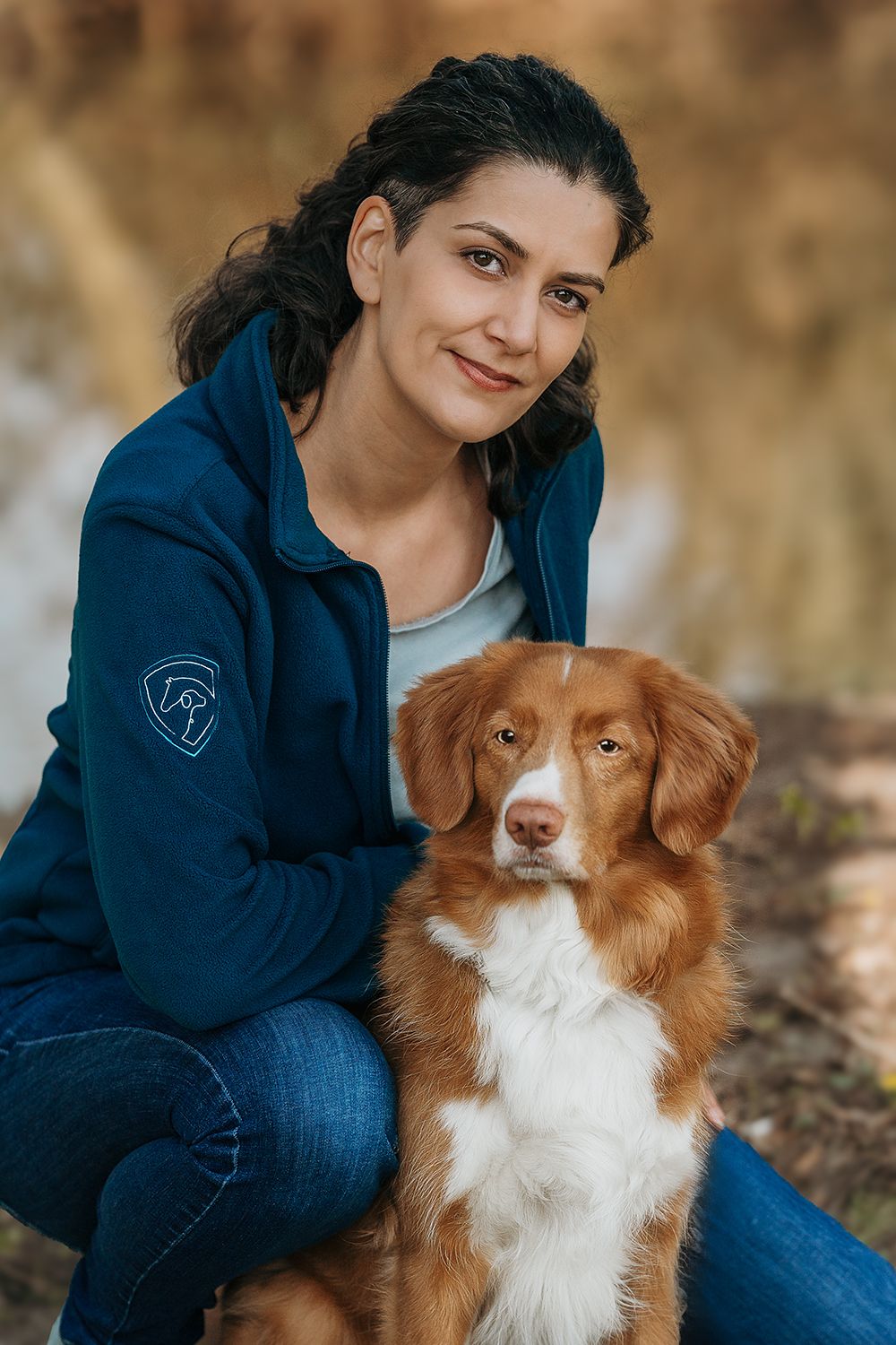Die Inhaberin von Tierische Verstärkung kniet locker auf dem Boden, ihr rot-weißer Retriever sitzt vor ihr.